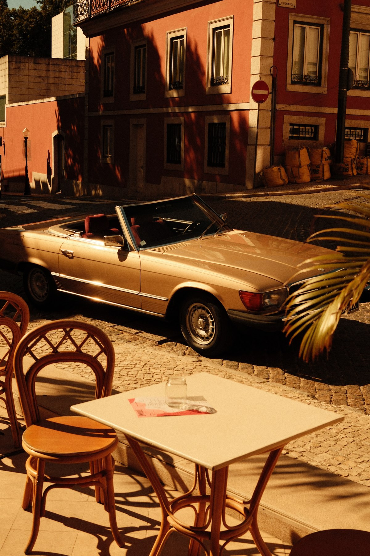 1982 Mercedes-Benz 380 SL rental Lisbon — side view on cobblestone street with café terrace